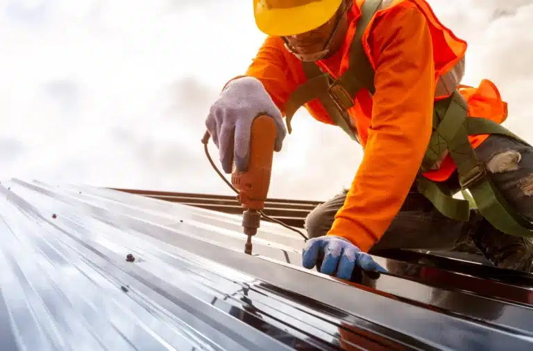 A worker using a nail gun secures underlayment on a wooden roof.